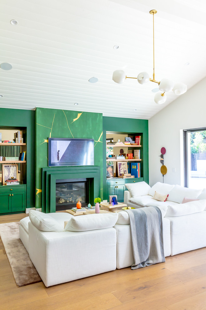Contemporary open concept family room in Los Angeles with green walls, medium hardwood floors, a standard fireplace, a wall-mounted tv and brown floor.