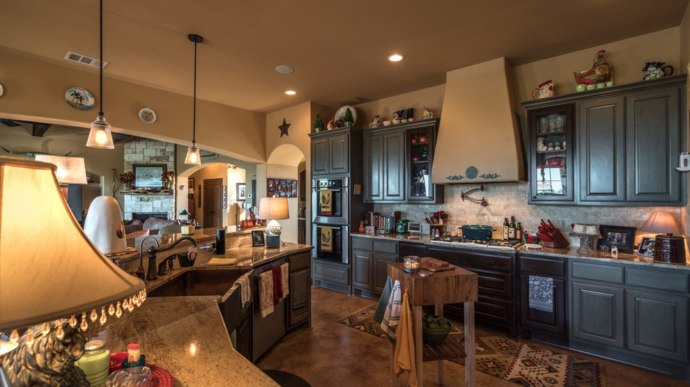 Inspiration for a large rustic l-shaped concrete floor eat-in kitchen remodel in Austin with a farmhouse sink, shaker cabinets, gray cabinets, granite countertops, beige backsplash, subway tile backsplash, stainless steel appliances and an island