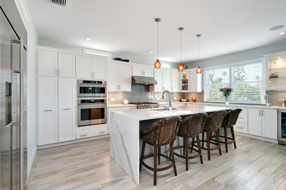 This is an example of a mid-sized transitional u-shaped open plan kitchen in Tampa with a double-bowl sink, recessed-panel cabinets, white cabinets, marble benchtops, grey splashback, cement tile splashback, stainless steel appliances, porcelain floors, with island and grey floor.