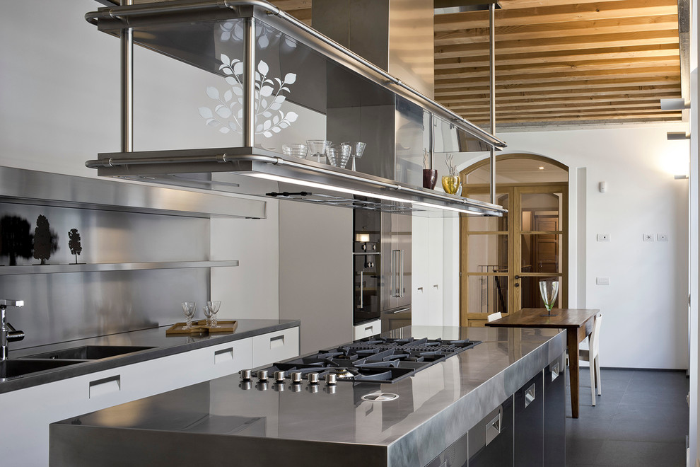 Design ideas for an industrial single-wall eat-in kitchen in Milan with an integrated sink, glass-front cabinets, stainless steel cabinets, stainless steel benchtops, metallic splashback and with island.