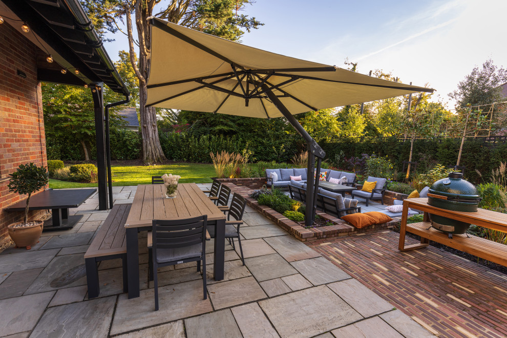Photo of a large contemporary back patio in Buckinghamshire with a bbq area, brick paving and an awning.
