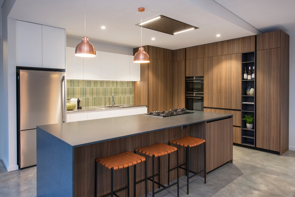 Moderne Küche in L-Form mit flächenbündigen Schrankfronten, hellbraunen Holzschränken, Küchenrückwand in Grün, Küchengeräten aus Edelstahl, Betonboden, Kücheninsel, grauem Boden und grauer Arbeitsplatte in Perth