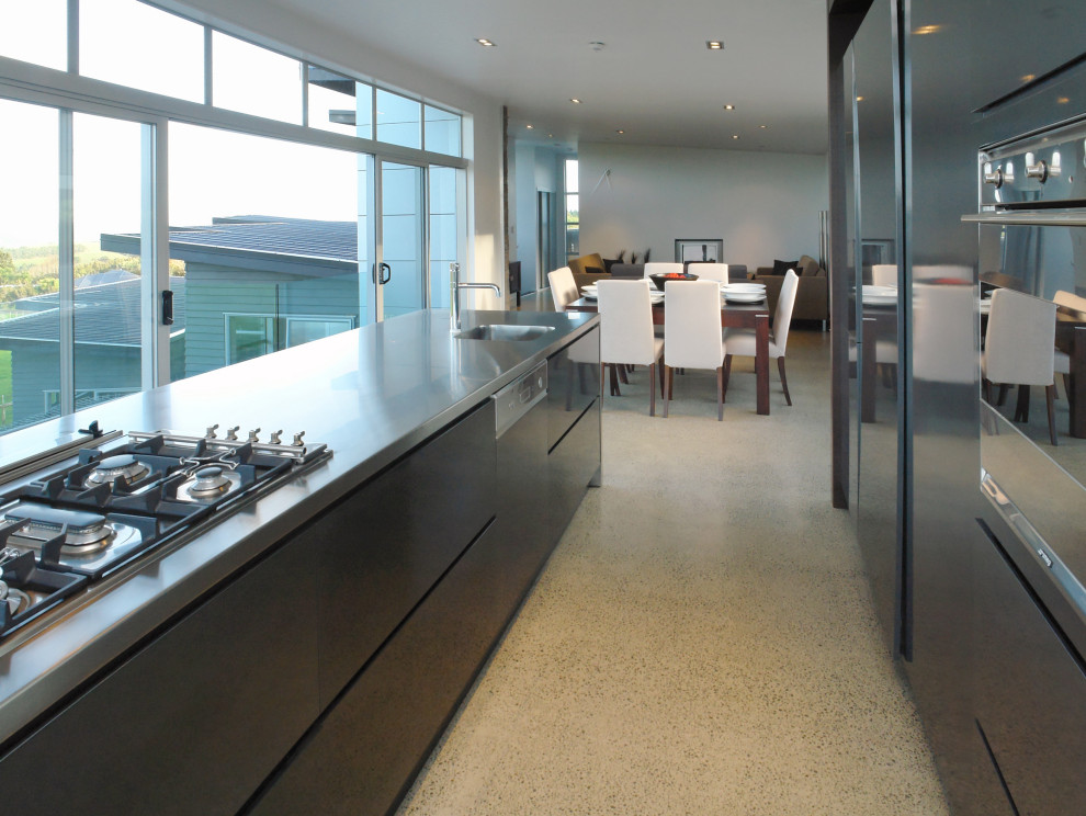 Large minimalist galley concrete floor and gray floor eat-in kitchen photo in Auckland with a single-bowl sink, flat-panel cabinets, gray cabinets, stainless steel countertops, stainless steel appliances, a peninsula and gray countertops