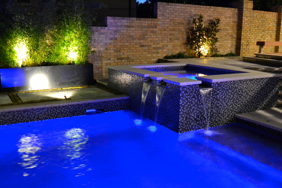 This is an example of a transitional backyard rectangular pool in Dallas with a water feature and natural stone pavers.