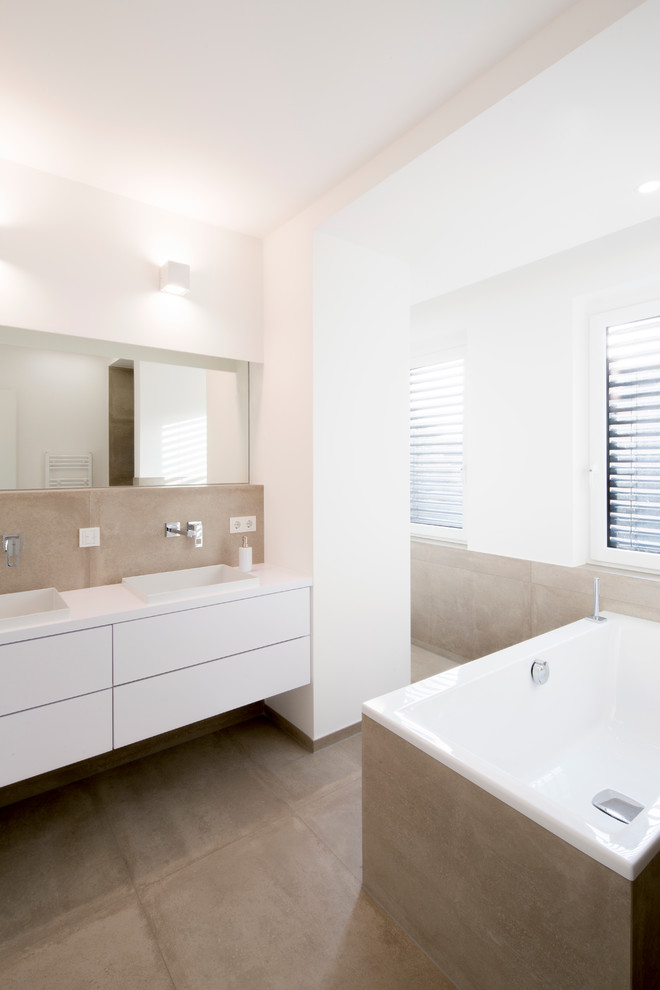 Mid-sized contemporary bathroom in Dusseldorf with flat-panel cabinets, white cabinets, a drop-in tub, white walls, concrete floors, stone slab and a drop-in sink.