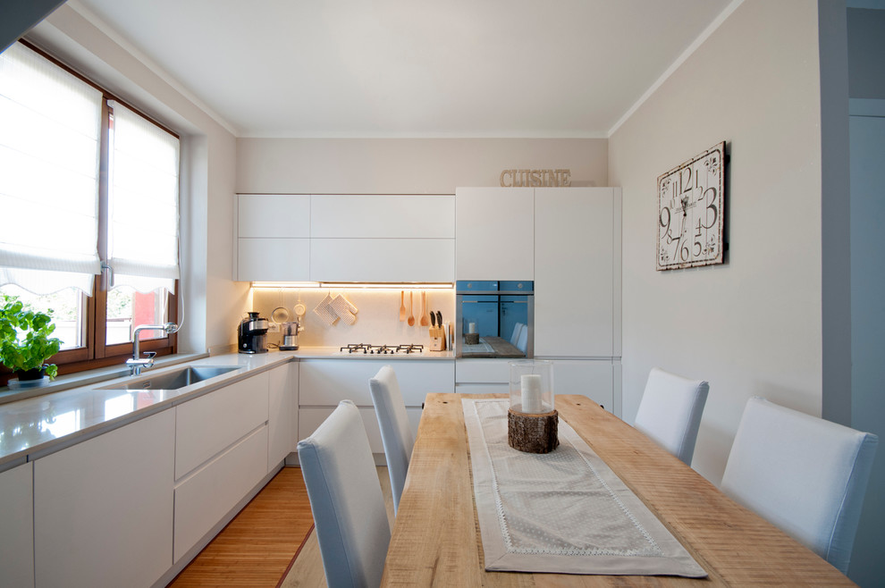 Design ideas for a large contemporary l-shaped eat-in kitchen in Milan with an undermount sink, flat-panel cabinets, white cabinets, white splashback, stainless steel appliances and light hardwood floors.
