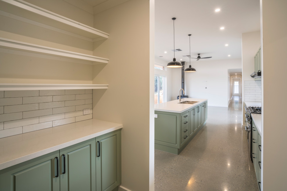 This is an example of a large contemporary galley kitchen pantry in Other with a drop-in sink, recessed-panel cabinets, green cabinets, quartz benchtops, white splashback, ceramic splashback, black appliances, concrete floors, with island, grey floor and white benchtop.