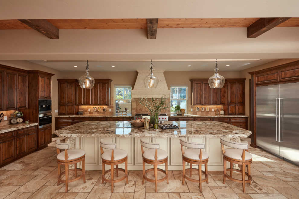 This is an example of an expansive mediterranean u-shaped open plan kitchen in San Francisco with a farmhouse sink, raised-panel cabinets, dark wood cabinets, granite benchtops, beige splashback, limestone splashback, stainless steel appliances, limestone floors, with island, beige floor, beige benchtop and exposed beam.