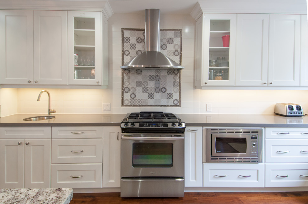 Inspiration for a large transitional u-shaped medium tone wood floor open concept kitchen remodel in Toronto with a drop-in sink, shaker cabinets, white cabinets, quartzite countertops, white backsplash, ceramic backsplash, stainless steel appliances and an island