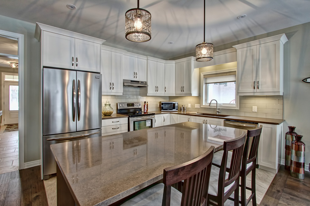 Inspiration for a large transitional l-shaped limestone floor open concept kitchen remodel in Toronto with an undermount sink, shaker cabinets, white cabinets, granite countertops, white backsplash, glass tile backsplash, stainless steel appliances and an island