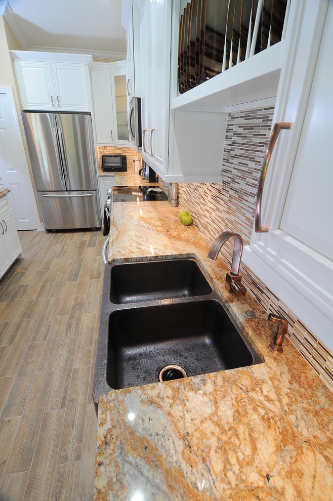 Kitchen pantry - transitional medium tone wood floor kitchen pantry idea in Miami with a farmhouse sink, raised-panel cabinets, white cabinets, granite countertops, multicolored backsplash, ceramic backsplash, stainless steel appliances and an island