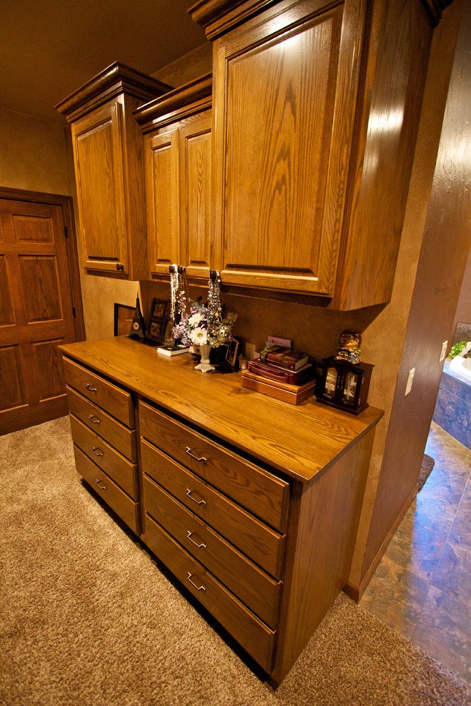 Walk-in closet - large gender-neutral carpeted walk-in closet idea with raised-panel cabinets and dark wood cabinets