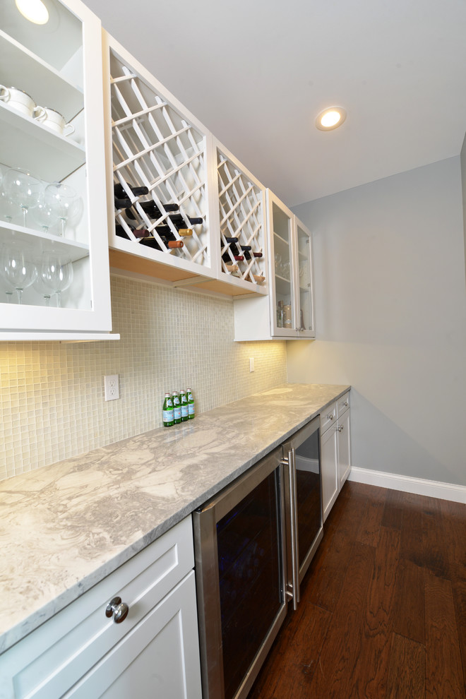 Design ideas for a mid-sized transitional single-wall wet bar in St Louis with shaker cabinets, white cabinets, marble benchtops, white splashback, glass tile splashback, dark hardwood floors, brown floor and grey benchtop.