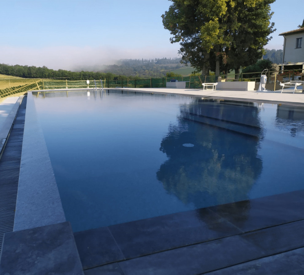 Large country courtyard rectangular infinity pool in Other with a pool house and tile.