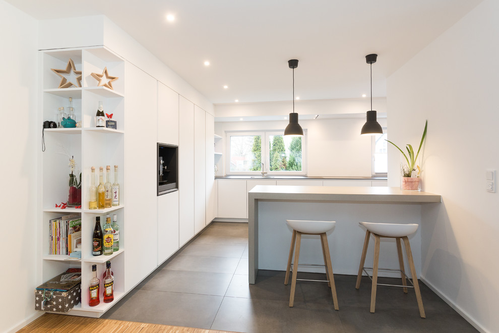 Design ideas for an expansive contemporary galley open plan kitchen in Frankfurt with a single-bowl sink, flat-panel cabinets, white cabinets, concrete benchtops, white splashback, black appliances and a peninsula.