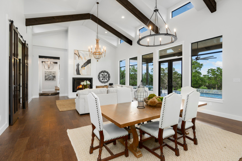 Photo of a mid-sized country open plan dining in Austin with white walls, dark hardwood floors, a hanging fireplace, a metal fireplace surround, brown floor and vaulted.