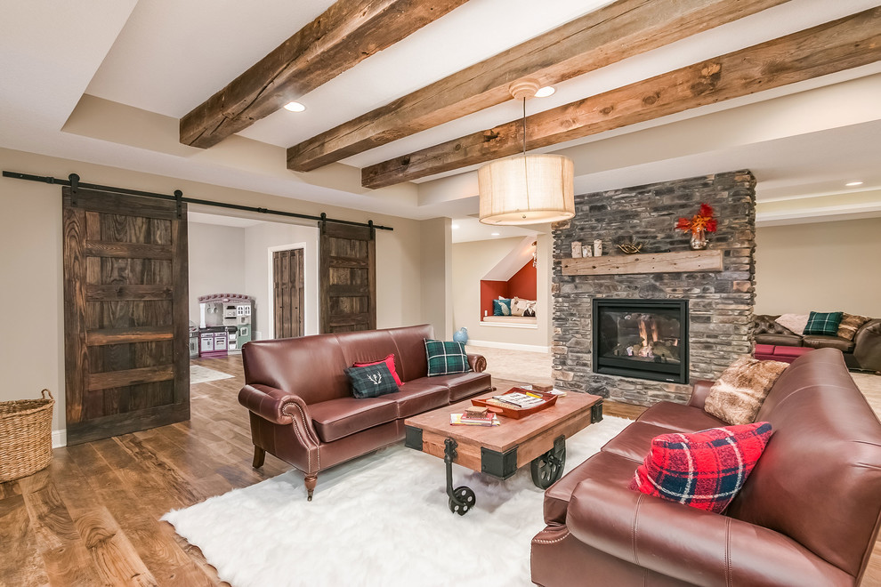 Inspiration for a mid-sized country walk-out basement in Minneapolis with beige walls, medium hardwood floors, a two-sided fireplace, a stone fireplace surround and brown floor.