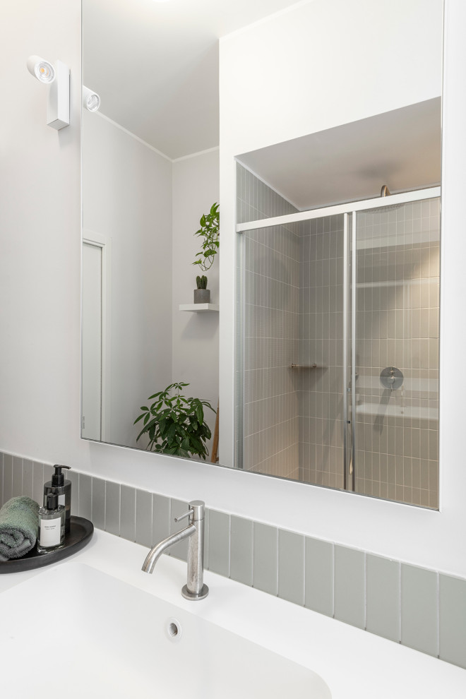 Inredning av ett modernt mellanstort vit vitt en-suite badrum, med släta luckor, gröna skåp, en dusch i en alkov, en vägghängd toalettstol, grön kakel, stickkakel, vita väggar, ljust trägolv, ett integrerad handfat, bänkskiva i akrylsten och dusch med skjutdörr