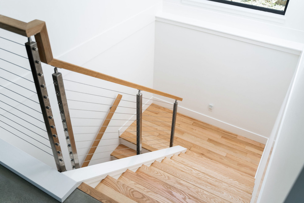 Example of a small minimalist wooden u-shaped cable railing staircase design in Vancouver with wooden risers
