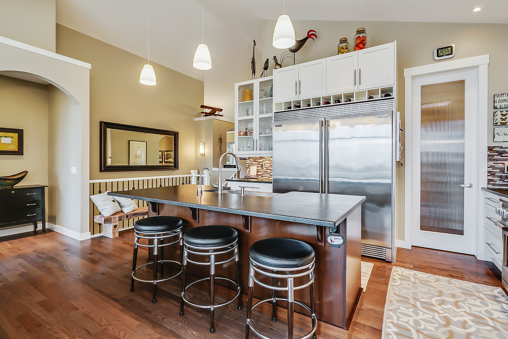 Mid-sized transitional galley eat-in kitchen in Calgary with a farmhouse sink, shaker cabinets, white cabinets, granite benchtops, multi-coloured splashback, stainless steel appliances, medium hardwood floors, no island, white benchtop, matchstick tile splashback and brown floor.