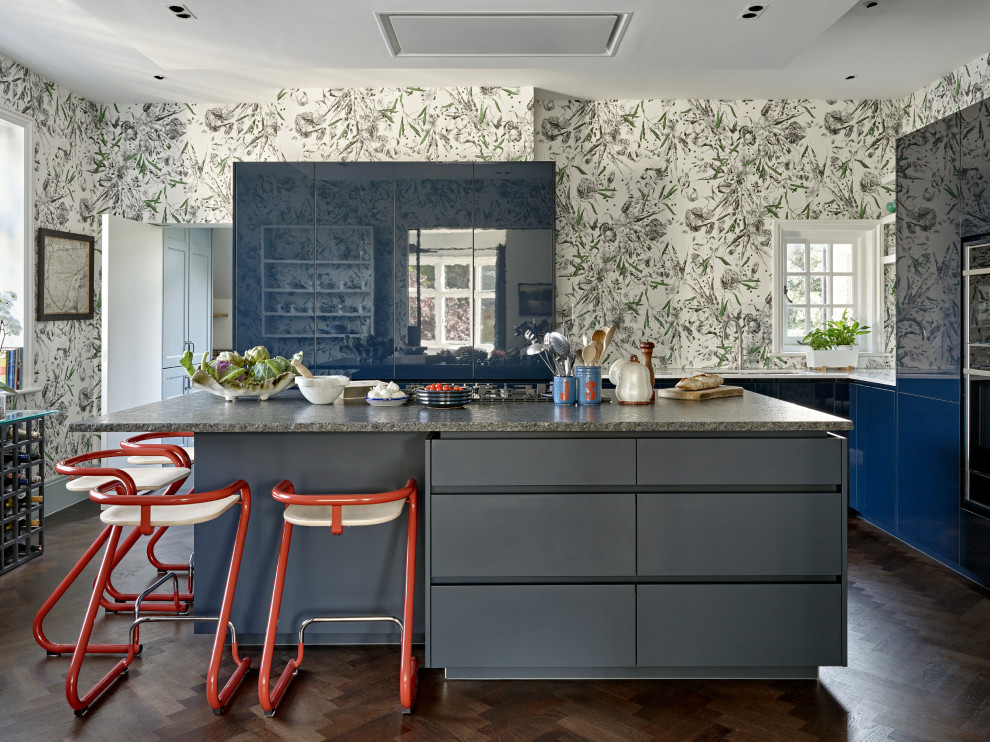 Eclectic u-shaped kitchen in London with flat-panel cabinets, blue cabinets, panelled appliances, dark hardwood floors, with island, brown floor, grey benchtop and wallpaper.