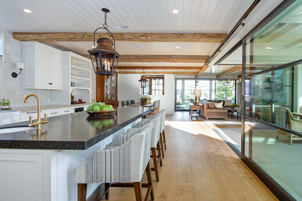 Example of a large cottage l-shaped light wood floor and brown floor eat-in kitchen design in Orange County with a farmhouse sink, shaker cabinets, white cabinets, quartzite countertops, beige backsplash, ceramic backsplash, stainless steel appliances, an island and beige countertops