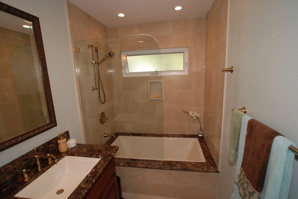 This is an example of a large modern master bathroom in Orange County with an undermount sink, raised-panel cabinets, dark wood cabinets, marble benchtops, an undermount tub, a shower/bathtub combo, a one-piece toilet, beige tile, stone tile, white walls and travertine floors.