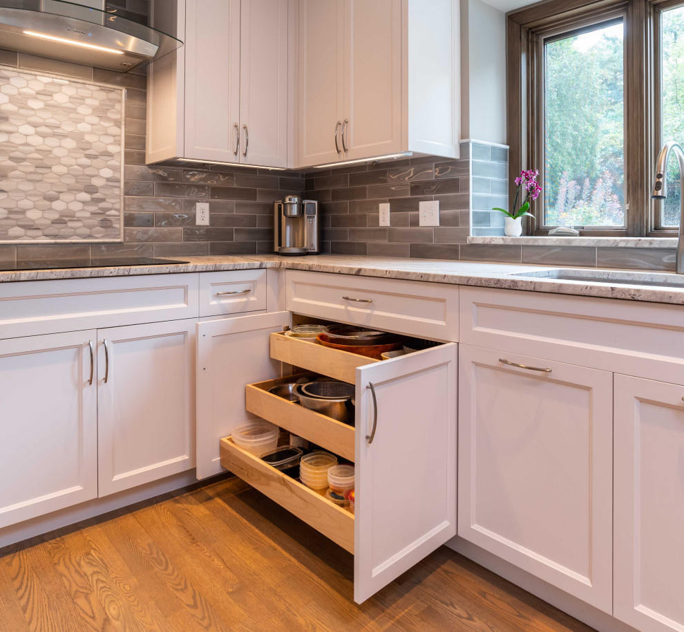 Photo of a mid-sized transitional u-shaped kitchen in Minneapolis with a single-bowl sink, shaker cabinets, white cabinets, granite benchtops, grey splashback, subway tile splashback, stainless steel appliances, medium hardwood floors, no island, brown floor and white benchtop.