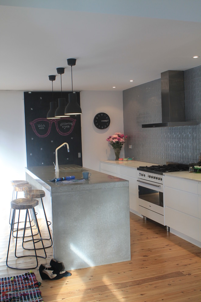 Inspiration for a mid-sized eclectic eat-in kitchen in Sydney with an integrated sink, flat-panel cabinets, white cabinets, concrete benchtops, grey splashback, metal splashback, white appliances, light hardwood floors and with island.