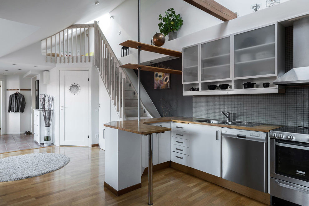 Design ideas for a scandinavian l-shaped open plan kitchen in Stockholm with a double-bowl sink, flat-panel cabinets, white cabinets, wood benchtops, grey splashback, mosaic tile splashback, stainless steel appliances, medium hardwood floors, a peninsula, brown floor and brown benchtop.