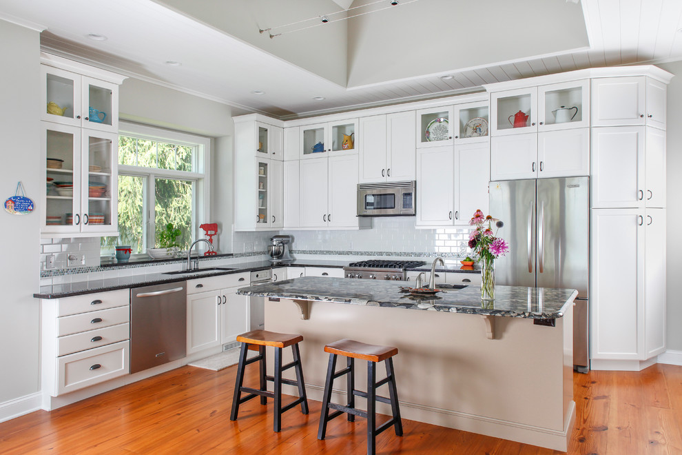 Inspiration for a large traditional l-shaped kitchen in Detroit with subway tile splashback, an undermount sink, white cabinets, white splashback, stainless steel appliances, granite benchtops, shaker cabinets, medium hardwood floors, with island and brown floor.