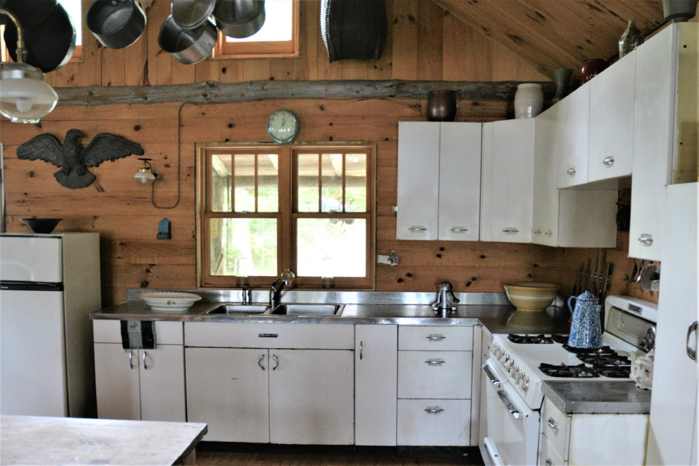 Mid-sized mountain style l-shaped light wood floor open concept kitchen photo with a drop-in sink, flat-panel cabinets, white cabinets, stainless steel countertops, brown backsplash, wood backsplash, white appliances and an island