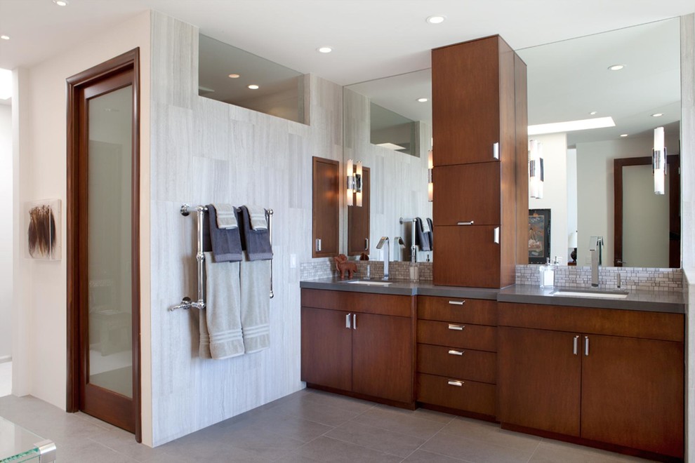 Photo of a large contemporary master bathroom in Los Angeles with an undermount sink, flat-panel cabinets, dark wood cabinets, solid surface benchtops, a freestanding tub, gray tile, white walls, porcelain tile, porcelain floors, grey floor, a one-piece toilet and grey benchtops.
