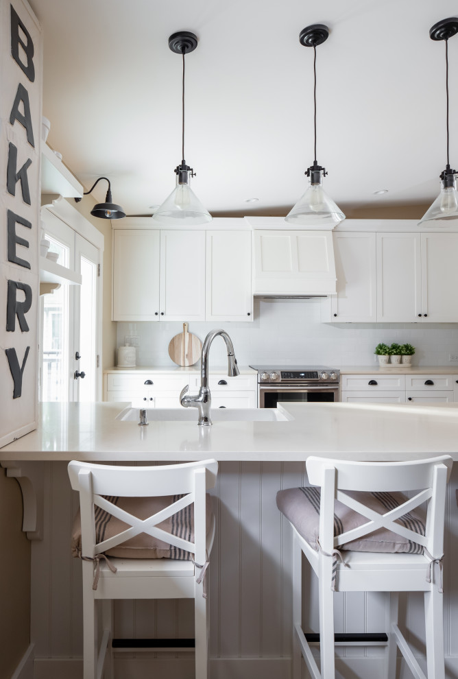 Example of a large mountain style l-shaped medium tone wood floor and brown floor eat-in kitchen design in Vancouver with a farmhouse sink, shaker cabinets, white cabinets, quartzite countertops, white backsplash, subway tile backsplash, stainless steel appliances, an island and white countertops