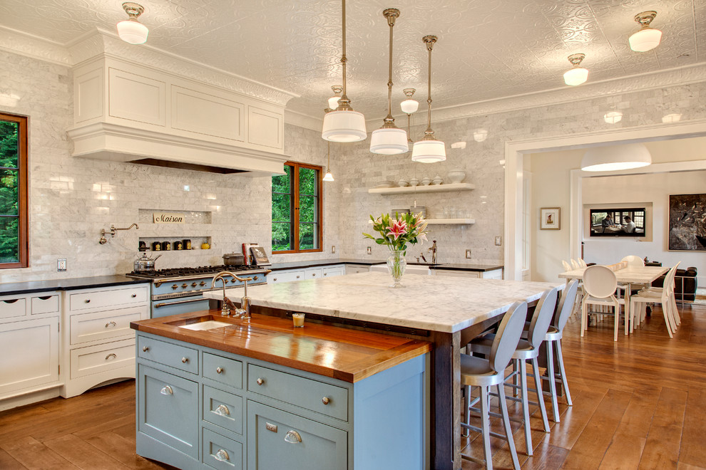Design ideas for an expansive traditional u-shaped separate kitchen in Seattle with a farmhouse sink, recessed-panel cabinets, white cabinets, marble benchtops, white splashback, stone tile splashback, white appliances, medium hardwood floors and with island.