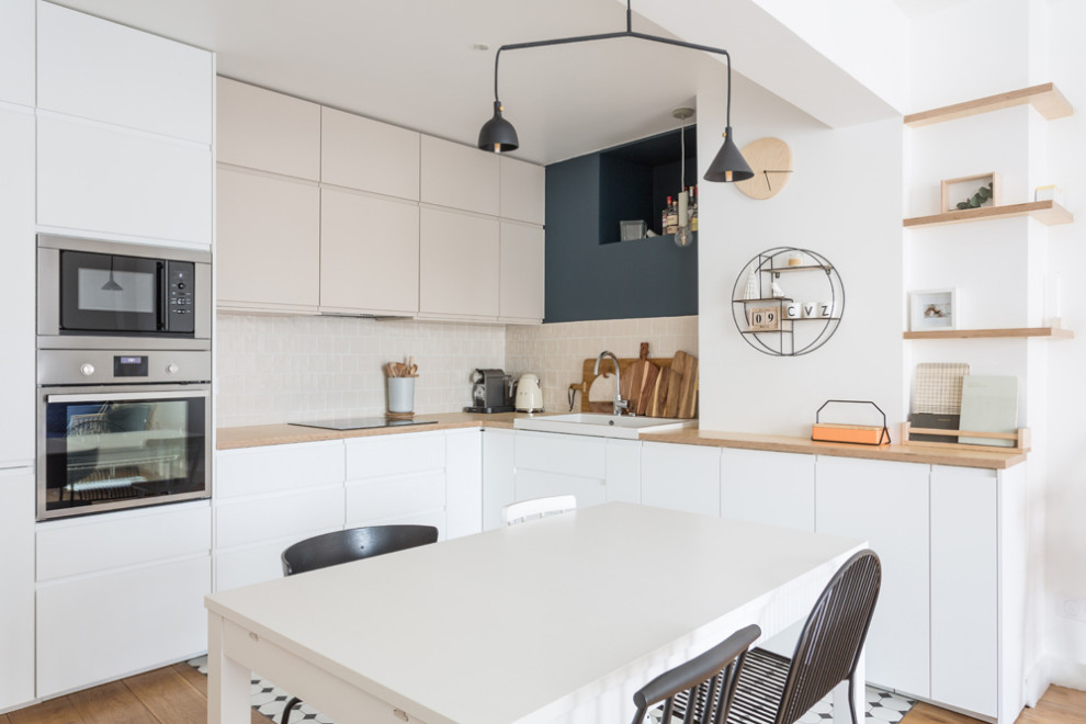 Large scandinavian l-shaped open plan kitchen in Paris with a single-bowl sink, beaded inset cabinets, white cabinets, wood benchtops, beige splashback, terra-cotta splashback, stainless steel appliances, porcelain floors, no island, multi-coloured floor and beige benchtop.