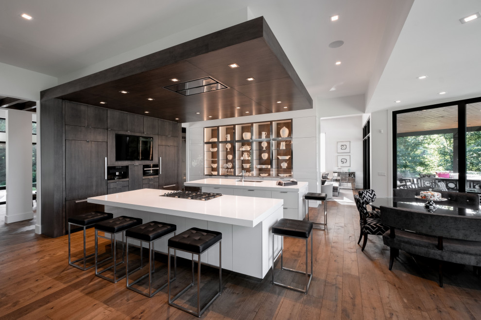 Photo of a large contemporary u-shaped eat-in kitchen in Other with an undermount sink, flat-panel cabinets, grey cabinets, quartz benchtops, panelled appliances, medium hardwood floors, multiple islands, brown floor and white benchtop.