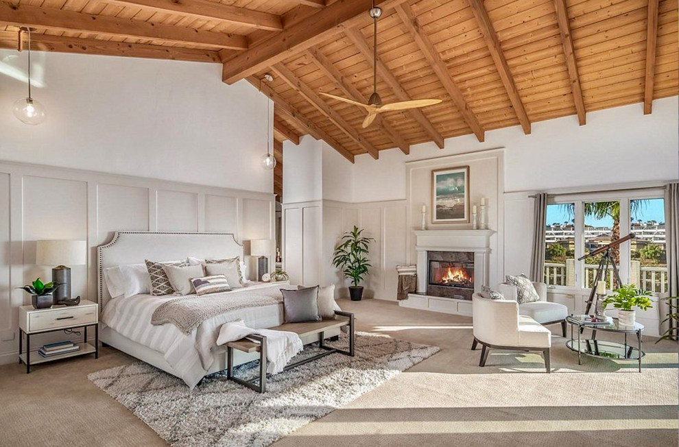This is an example of an expansive transitional master bedroom in San Diego with white walls, carpet, a standard fireplace, a plaster fireplace surround, beige floor and vaulted.