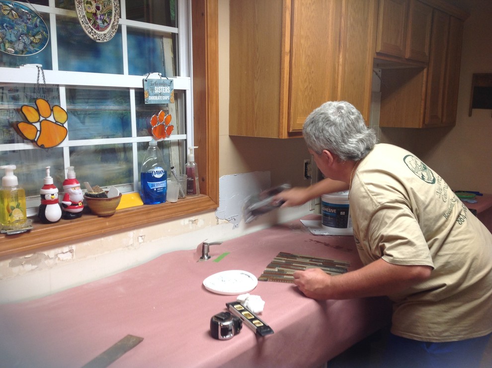 Example of a l-shaped eat-in kitchen design with an undermount sink, flat-panel cabinets, brown backsplash, glass tile backsplash, stainless steel appliances and a peninsula