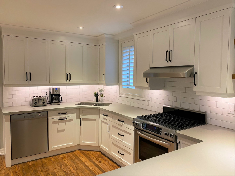 Example of a mid-sized transitional u-shaped medium tone wood floor and brown floor open concept kitchen design in Toronto with an undermount sink, shaker cabinets, white cabinets, quartz countertops, white backsplash, porcelain backsplash, stainless steel appliances, a peninsula and gray countertops