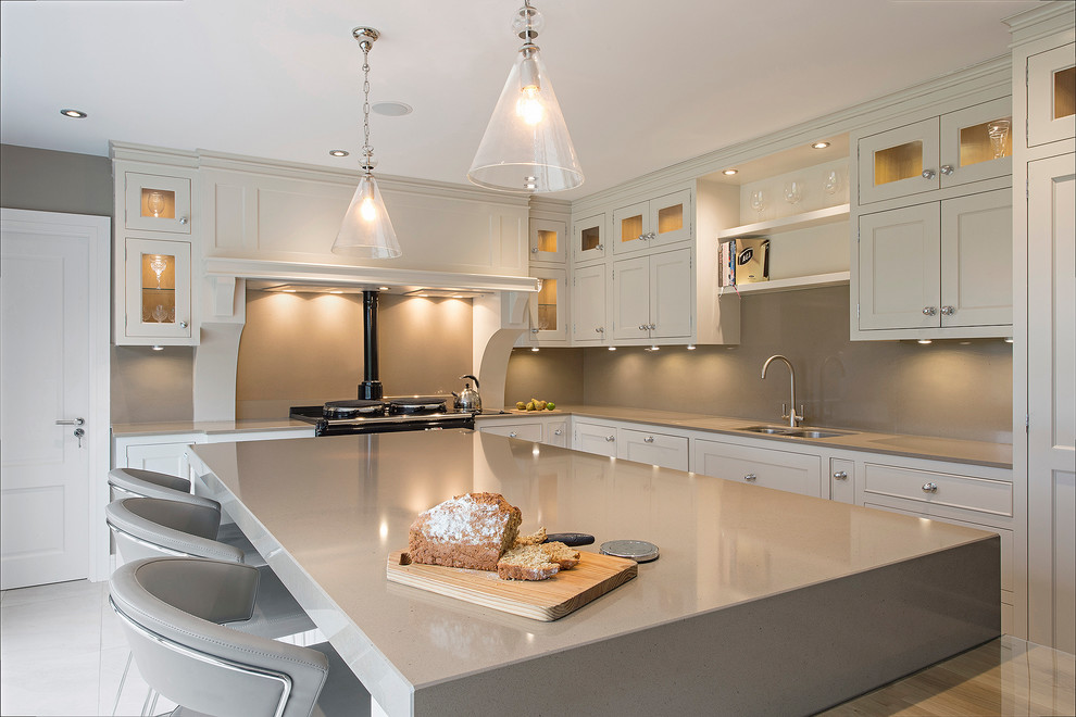 Transitional l-shaped open plan kitchen in Dublin with a double-bowl sink, recessed-panel cabinets, white cabinets, soapstone benchtops, beige splashback, glass sheet splashback, panelled appliances, ceramic floors and with island.