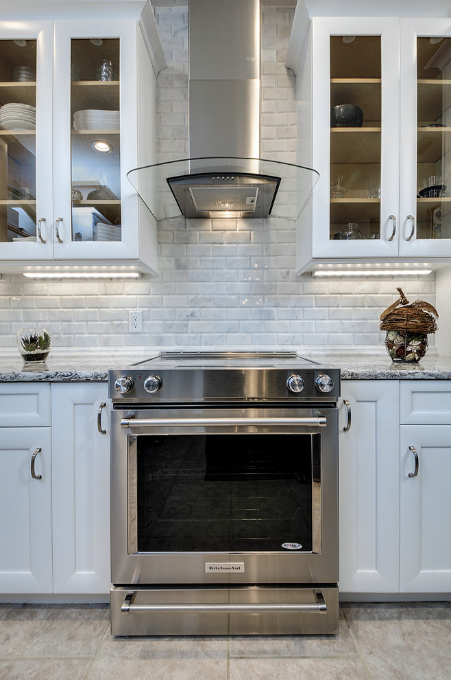 Example of a transitional ceramic tile kitchen design in Tampa with a farmhouse sink, white cabinets, white backsplash, stone tile backsplash, stainless steel appliances and an island