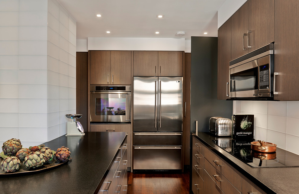 Design ideas for a small contemporary kitchen in New York with flat-panel cabinets, dark wood cabinets, white splashback, stainless steel appliances, dark hardwood floors and with island.