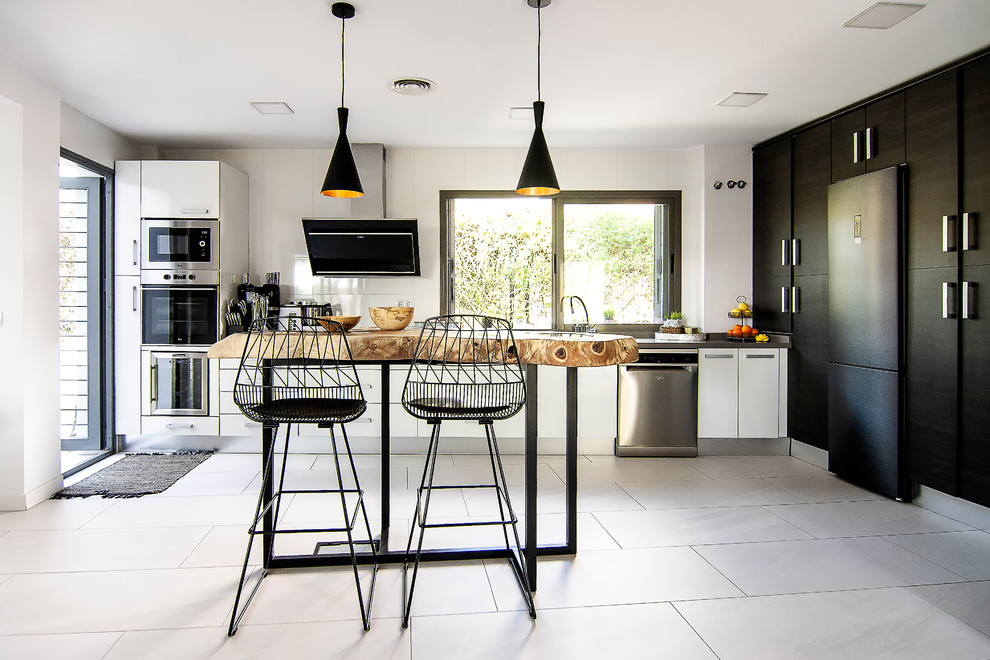 Inspiration for an eclectic open plan kitchen in Seville with an undermount sink, flat-panel cabinets, white cabinets, quartz benchtops, white splashback, ceramic splashback, stainless steel appliances, ceramic floors, with island, white floor and grey benchtop.