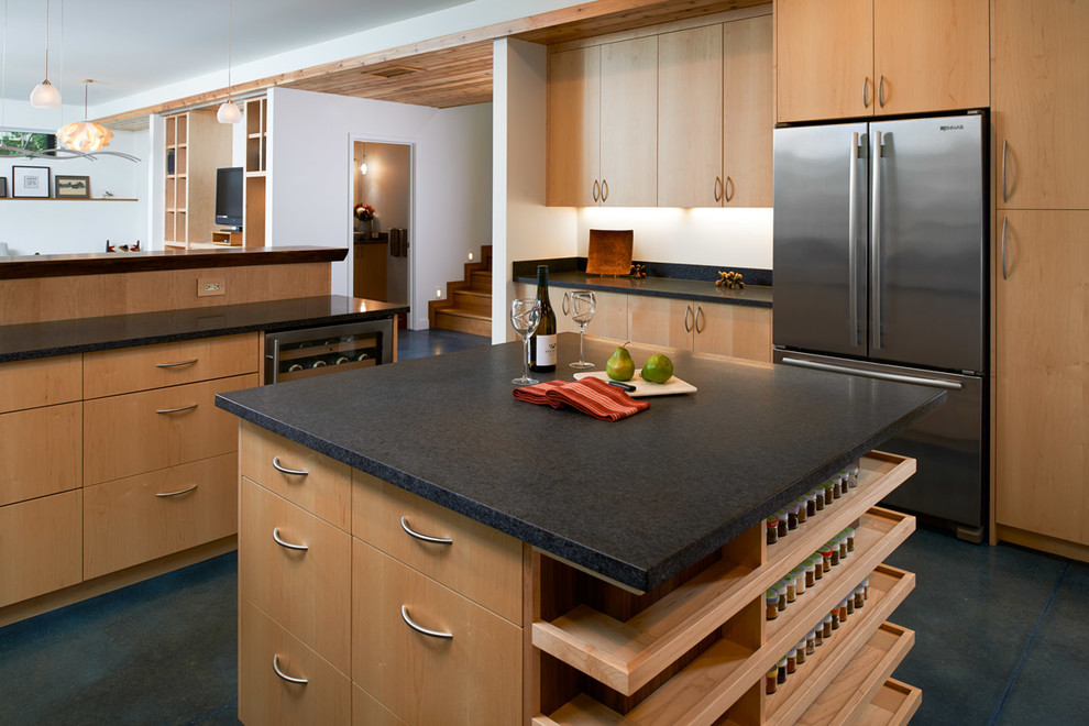 This is an example of a mid-sized contemporary u-shaped open plan kitchen in Detroit with flat-panel cabinets, light wood cabinets, granite benchtops, stainless steel appliances, concrete floors, with island, blue floor and black benchtop.