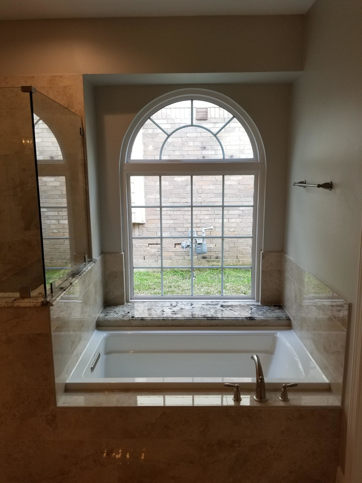 This is an example of a mid-sized transitional master bathroom in Houston with a drop-in tub, an alcove shower, white tile, marble, beige walls, pebble tile floors, granite benchtops, brown floor, a hinged shower door and beige benchtops.