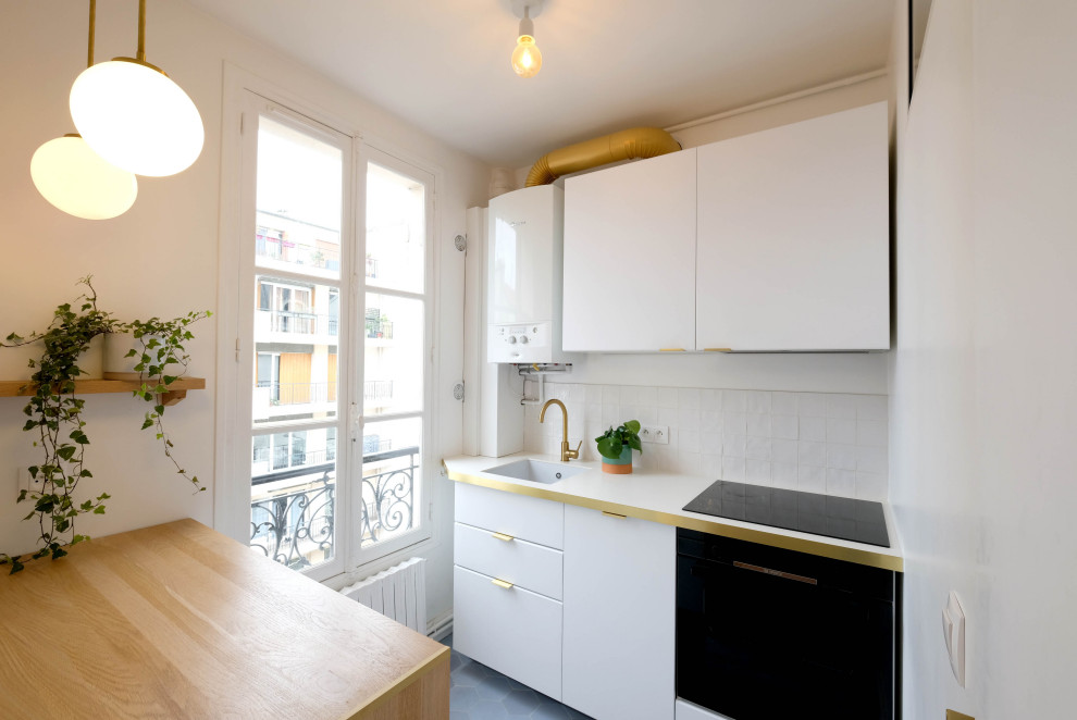 パリにあるお手頃価格の小さなミッドセンチュリースタイルのおしゃれなキッチン (アンダーカウンターシンク、フラットパネル扉のキャビネット、白いキャビネット、ラミネートカウンター、白いキッチンパネル、セラミックタイルのキッチンパネル、パネルと同色の調理設備、セメントタイルの床、青い床、白いキッチンカウンター) の写真