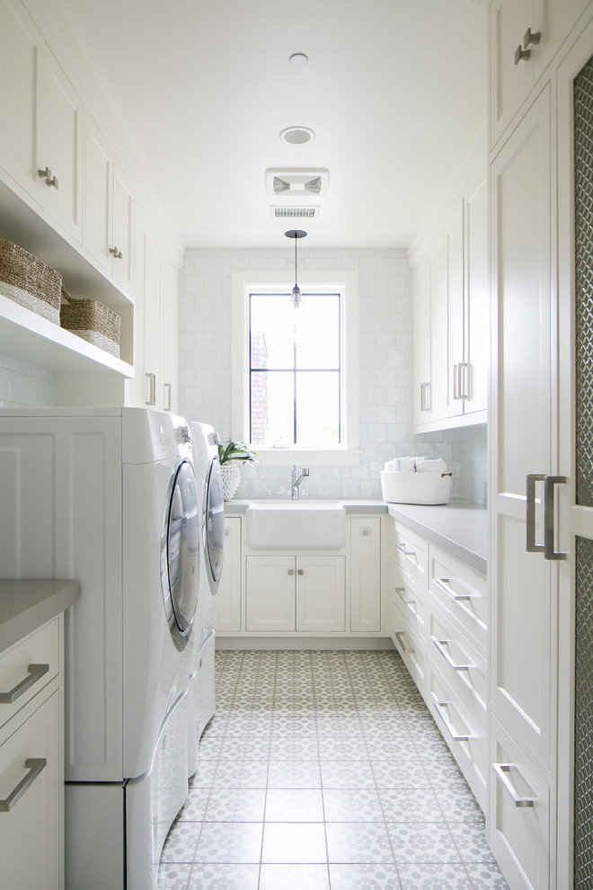 Photo of a beach style u-shaped dedicated laundry room in Orange County with a farmhouse sink, recessed-panel cabinets, white cabinets, white walls, a side-by-side washer and dryer, white floor and grey benchtop.