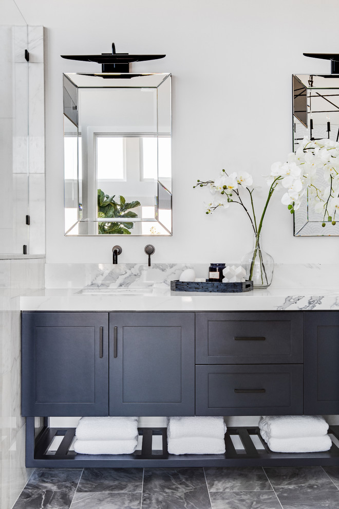 Inspiration for a mid-sized beach style master bathroom in Los Angeles with shaker cabinets, blue cabinets, a freestanding tub, an alcove shower, a two-piece toilet, white tile, marble, white walls, marble floors, an undermount sink, engineered quartz benchtops, grey floor, a hinged shower door and white benchtops.