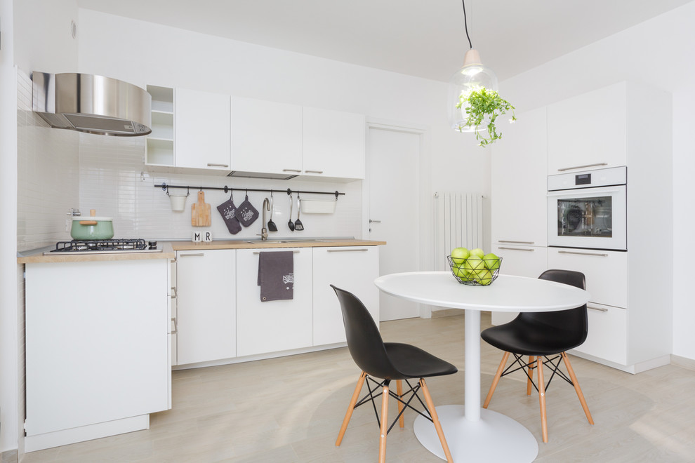 Inspiration for a small scandinavian l-shaped eat-in kitchen in Rome with flat-panel cabinets, white cabinets, white splashback, white appliances, light hardwood floors, no island and beige floor.
